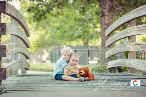 two brothers sitting on a wooden bridge with a teddy bear